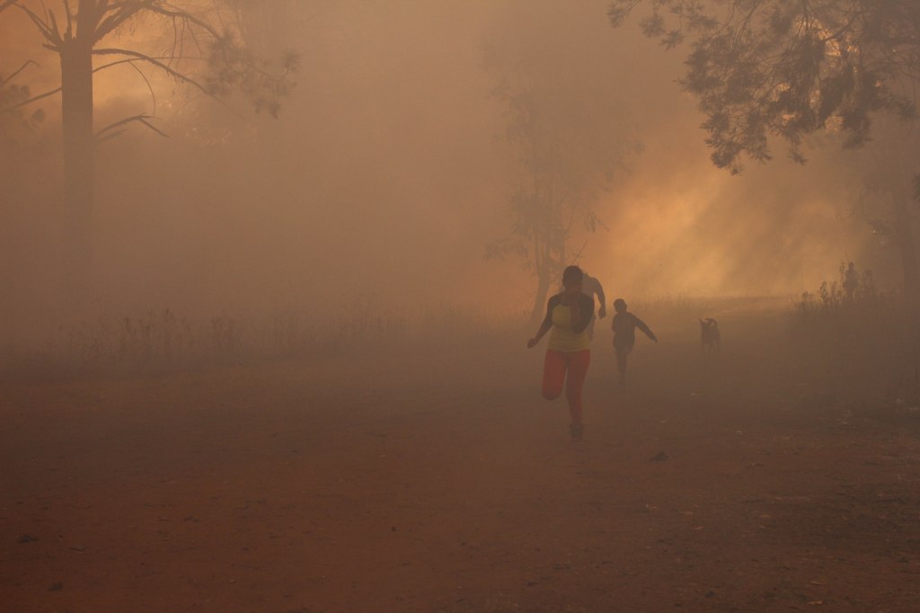 SOUTH AFRICA: A family runs under a cloud of smoke while covering their noses, as they make their way to their house, in Mapleton Extension 12 near Governors Catholic Church, on Flanagan Road, near the R103. Sunday, 21 June 2015. Just a stone's throw away from were the fire was most intense, residents of the nearby house alleged that the fire may have been started by children while playing in the nearby veld. © JABULILE PEARL HLANZE